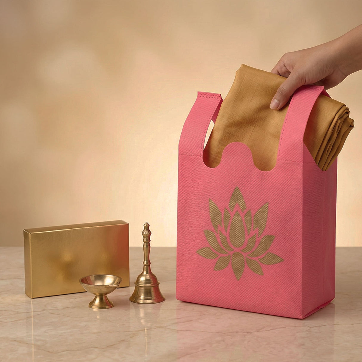 Pink reusable non woven tote bag with gold lotus design holding folded golden fabric for indian wedding puja