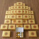 Golden-yellow rectangular sweet boxes with red and green mandala design arranged in pyramid for indian sweets gift