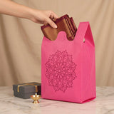 A vibrant pink reusable non woven tote bag with mandala print holding maroon and gold fabric for Indian weddings