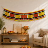 A vibrant multi-colored pom-pom jumbo marigold jasmine door toran hanging valance with yellow red green and white stripes
