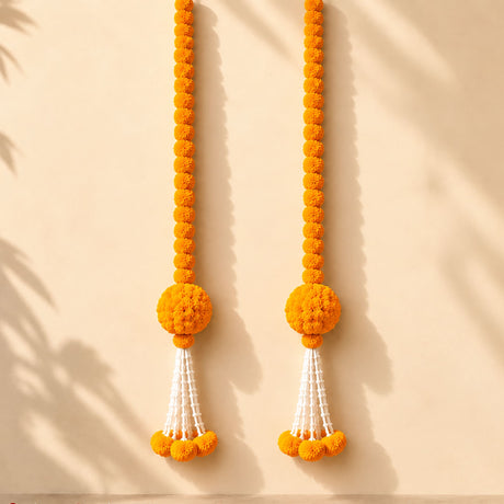 Two vibrant orange artificial marigold and jasmine hanging jhoomer garlands with pom-poms and white tassels for decoration
