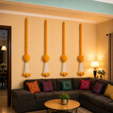 Four vertical orange marigold garland hanging jhoomers with white tassels displayed on beige wall for festive decor