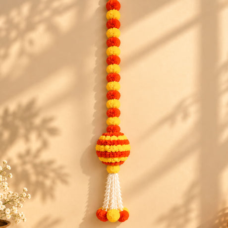 A vibrant orange and yellow artificial marigold hanging jhoomer garland with a striped spherical centerpiece and tassels for festive decor