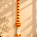 A vibrant orange and yellow artificial marigold hanging jhoomer garland with a striped spherical centerpiece and tassels for festive decor