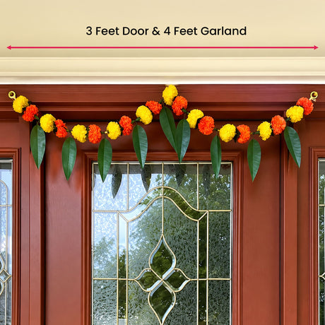 A vibrant orange and yellow artificial marigold flower and mango leaf garland on a red door for festive decor