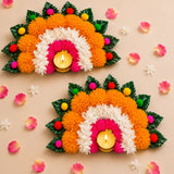 Vibrant orange white and pink marigold rangoli mat with artificial leaves framing two lit tea light candle holders for diwali decor