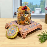 Copper decorative stand with floral design holding glass jar of assorted dried fruits