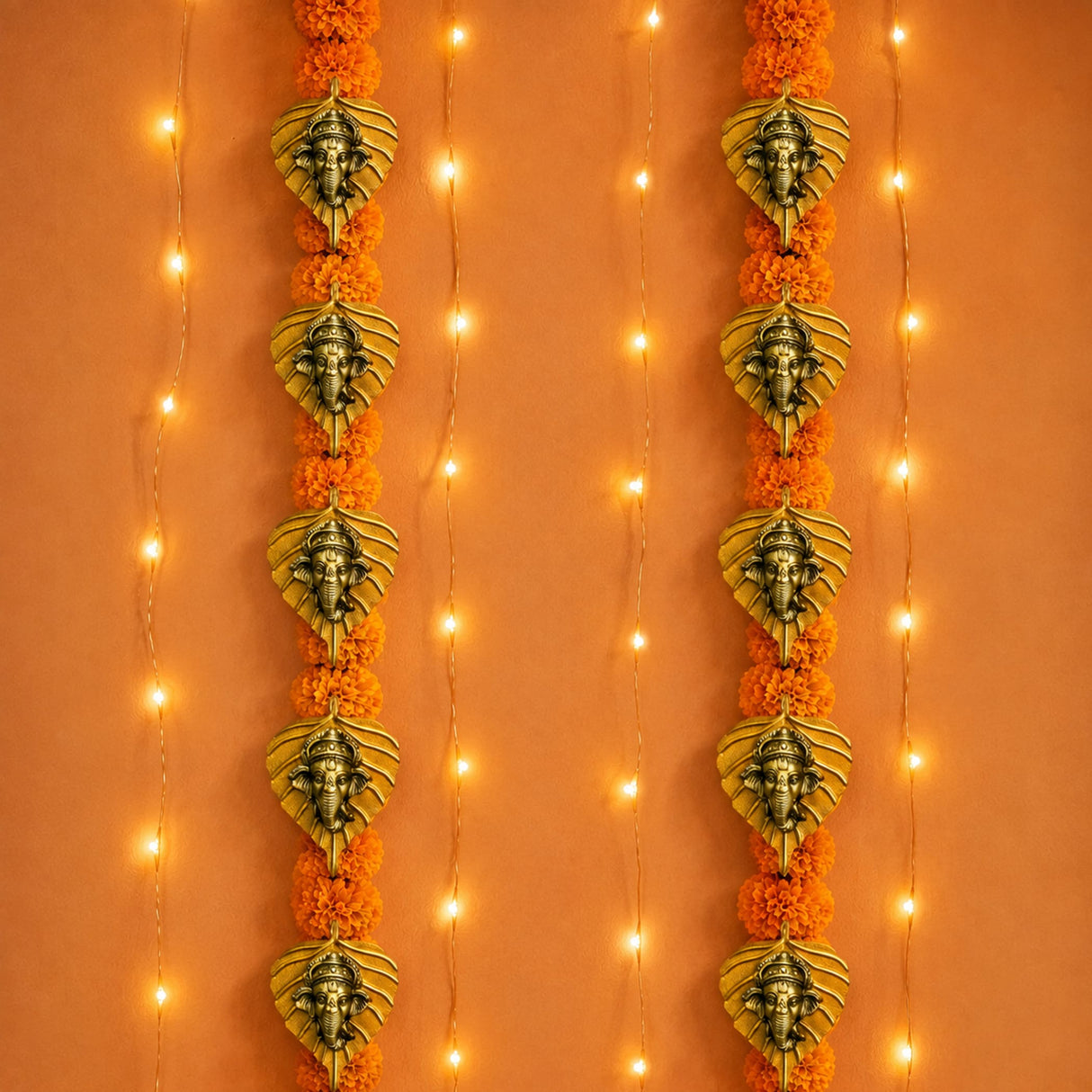 Metal leaf ganesha wall hanging decor featuring golden ganesha head ornaments adorned with orange marigold flowers