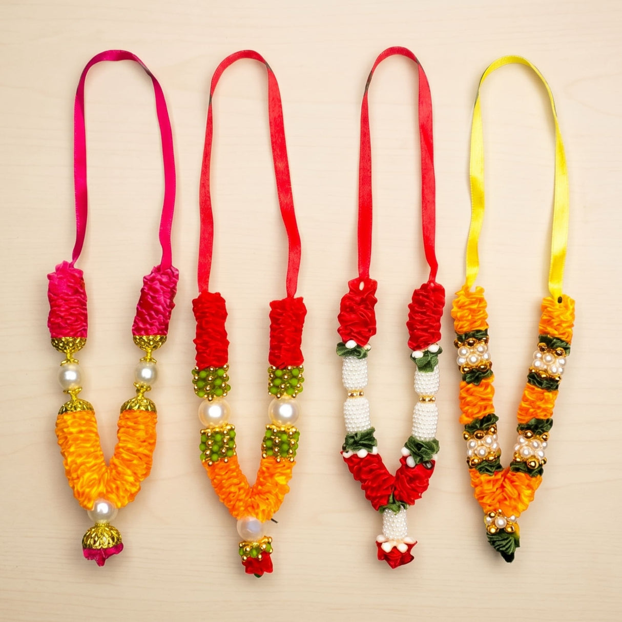 Four colorful 4 inches mini idol mala with vibrant orange and red fabric flowers, pearls, gold beads, and tassels for Diwali puja