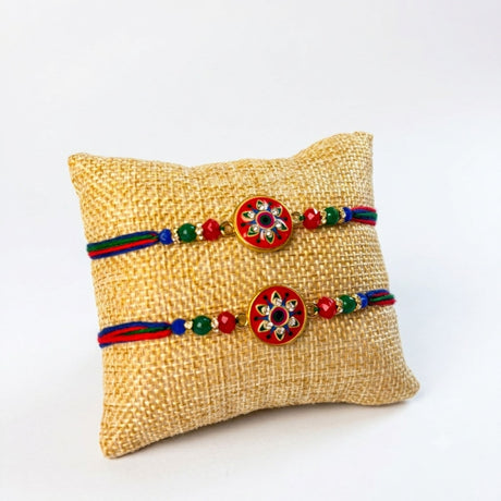 Two handcrafted designer rakhi bracelets with red enamel floral charms and multicolor braided threads for brother and bhabhi