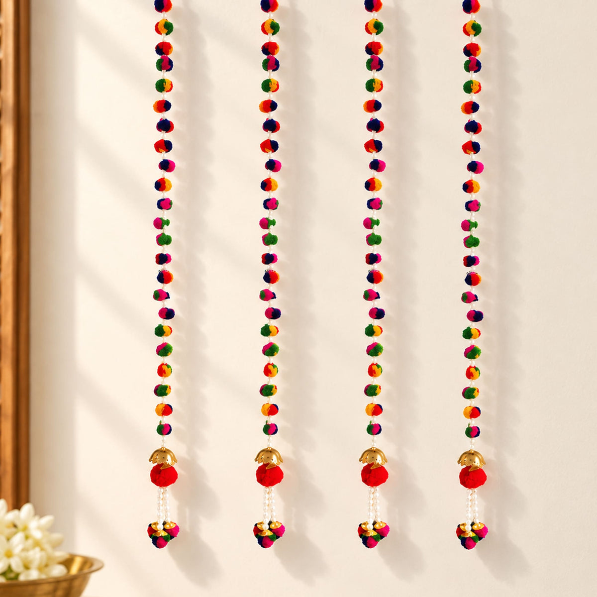 Four colorful pompom garland strings with red pompoms and gold bells for diwali and indian wedding decoration
