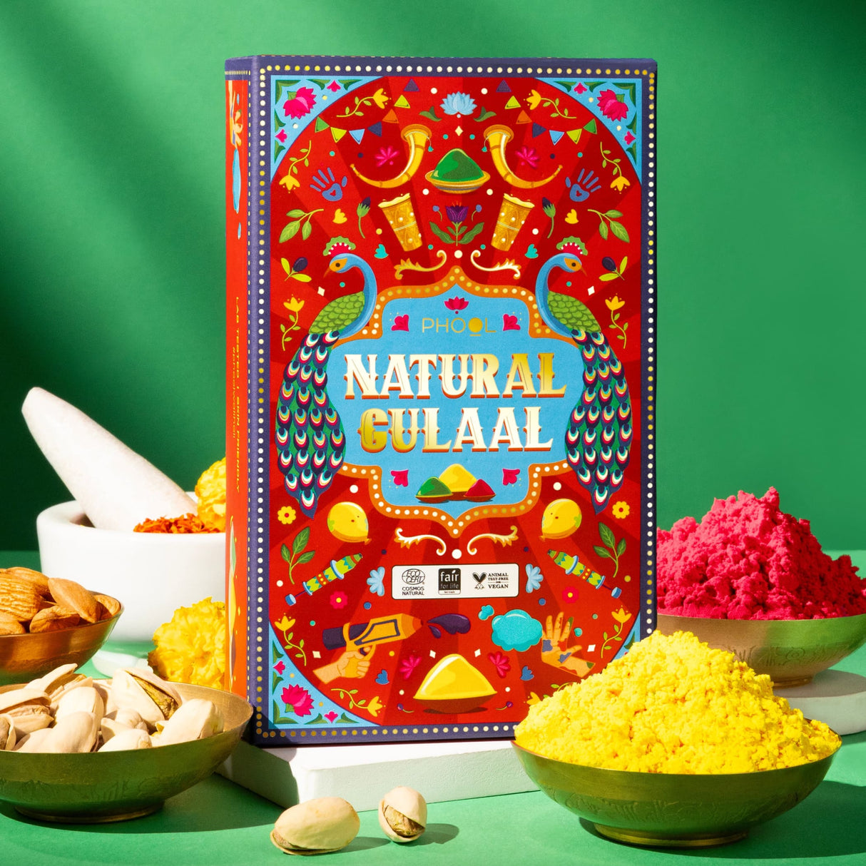 Vibrant red box of natural Holi gulal powder with peacock designs and greeting card