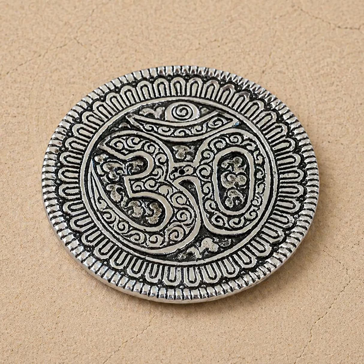 Silver-colored om aluminum incense holder disc with intricate engravings and textured border for temple decor and gifts