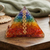 Orgonite pyramid filled with rainbow-colored crystal chips and adorned with a golden chakra symbol for spiritual healing