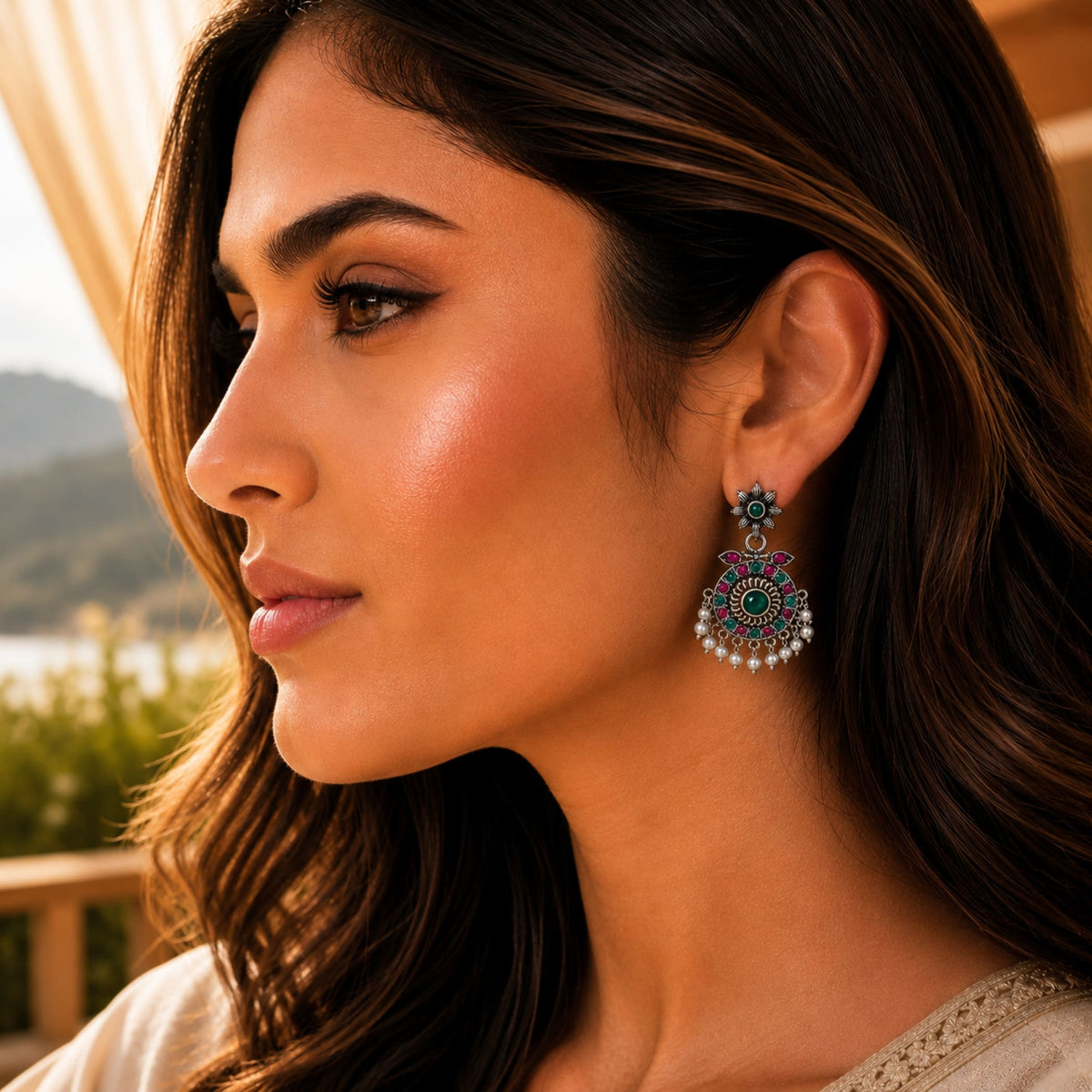 A woman wears Indian oxidized floral chandbali earrings with green gemstone red and blue stones accented by white pearls