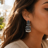 Silver oxidized floral jhumka earrings with intricate filigree, blue stone center, and dangling faux pearl beads for ethnic wear