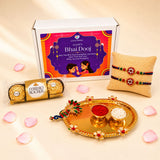 Golden ornate peacock puja plate with floral designs holding bowls of red powder and white rice for bhai dooj gift hamper set