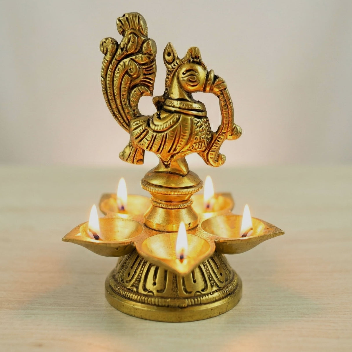 Golden brass diya with intricate peacock design and five lit oil lamps for diwali puja home decor and religious use