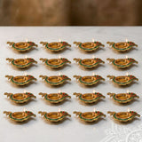 Golden brass diya lamps with green and red accents lit with small flames for diwali puja home decor and gifts
