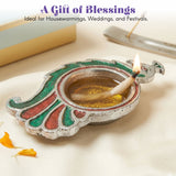 Silver brass finish peacock-shaped diya with green and red enamel accents holding a lit oil lamp for Diwali puja