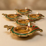 Gold-colored brass peacock deepam oil lamps with intricate green and red enamel designs lit for Diwali puja decor