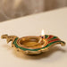 A golden brass peacock deepam diya with green and red enamel detailing lit for diwali puja and home decor