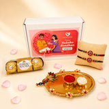 Gold-colored ornate decorative peacock handle tray holding bowls of red powder and white rice in peacock rakhi gift hamper set