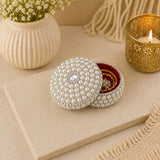 A round pearl-encrusted jewelry box with a diamond accent and red velvet interior for travel and gifting
