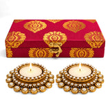 Red and gold patterned fabric box with golden clasp and two ornate gold diya holders with clear crystals for diwali gifts