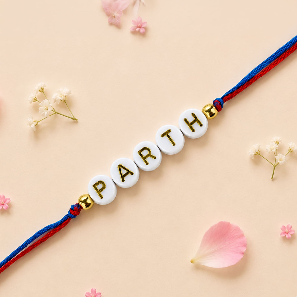 Designer custom named rakhi with white circular beads and gold lettering on red and blue cord for brother and bhabhi