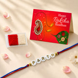 A personalized white bead rakhi with gold lettering spelling Parth and red and blue braided cord for Raksha Bandhan