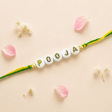 Designer custom named white beaded rakhi with gold pooja lettering and green yellow braided cord for protection and good luck