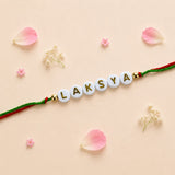 Designer custom named rakhi with white beads and gold lettering on red and green braided cord for protection and good luck