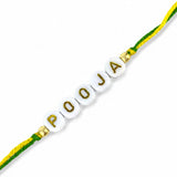 Designer custom named rakhi with white ceramic beads and gold lettering on green and yellow braided cord for raksha bandhan