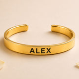 Gold-colored personalized stainless steel cuff bracelet with alex engraved in black for raksha bandhan gift
