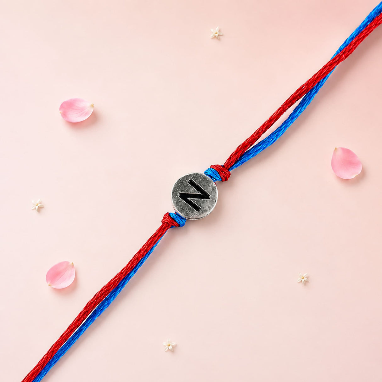 A silver circular charm with black engraved letter n on red and blue braided rakhi bracelet for brother and bhabhi
