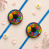 Two colorful circular fruit-themed pin wheel rakhis with black centers symbolizing protection and good luck