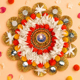 A vibrant circular tea light candle holder rangoli mat with gold foil fans red yellow pom-poms and a central lit diya