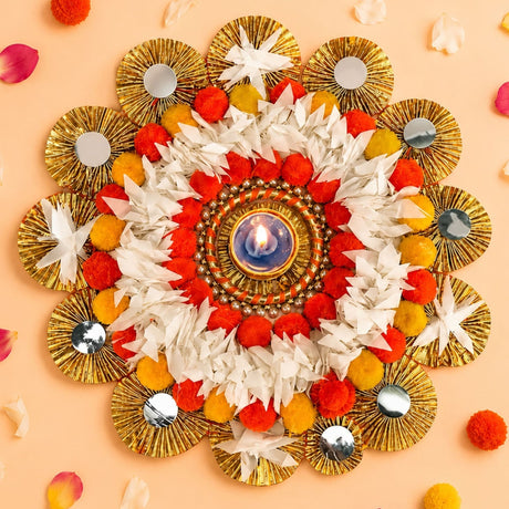 Tea light candle holder rangoli mat with gold foil fans, red white pom-poms, yellow flowers, and glowing oil lamp centerpiece