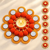 Ornamental rangoli mat tealight candle holder with central lit diya, orange pom-poms, and gold-rimmed mirrors for festive decor