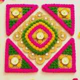 Rangoli mat with vibrant pink green yellow pom-poms gold accents and lit tea light candle holder for festive decor