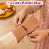 A maroon and gold rudraksha rakhi bracelet with wooden beads and metallic accents for raksha bandhan gift hamper