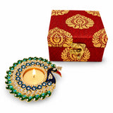 A vibrant peacock-themed diya with a golden base and green and blue gemstones in a premium diwali gift hamper box