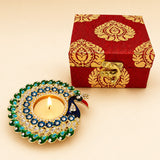 A vibrant peacock-themed diya with green and blue enamel and rhinestones in a premium Diwali gift hamper box