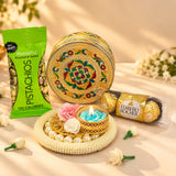 Gold-colored ornate round stainless steel sweet box with intricate red green and yellow meenakari floral enamel designs for festive gifting