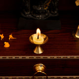 A golden brass oil lamp with a lit yellow candle featuring a flared base for pure cow ghee pooja diya wick use