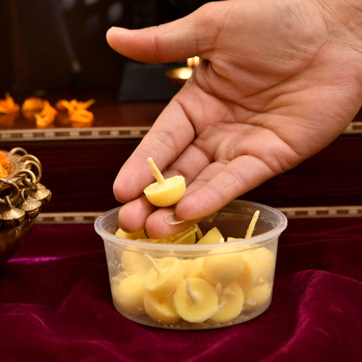 Hand holding a small pale yellow disc-shaped pure cow ghee diya wick with thin cotton wick for pooja and pujan use