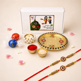 Gold-colored ornate rakhi with red and white gemstones on red thread included in rakhi gift hamper for brother with meenakari pooja thali set