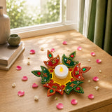 A vibrant red and green decorative rangoli diya with gold embroidery, swastika symbols, gemstones, and a glowing tea light candle