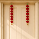 Red marigold toran garland with red pom-poms and gold bells hanging from a door for indian wedding and diwali decor